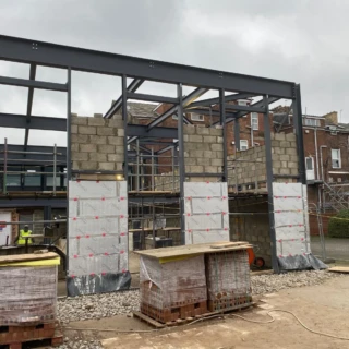 Ground-level view of a commercial extension featuring structural steel beams and masonry.