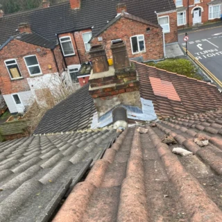 Close-up of concrete roof tiles, lead flashing, and a brick chimney stack requiring repairs in Hull.