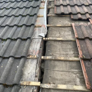 Roof restoration in progress showing new breathable membrane next to older tile underlayment along a party wall gap.