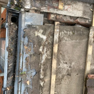 Top-down view of worn, deteriorating roof felt and timber rafters above a property gutter.