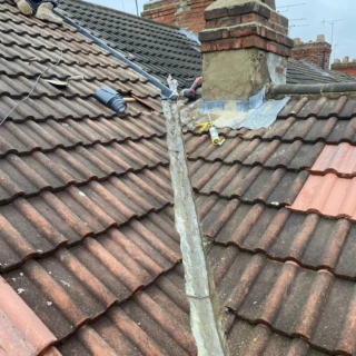 Roofer working near a brick chimney stack with lead flashing roll and valley trough in place.