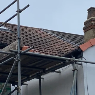 Ground-up perspective through scaffolding showing a newly tiled roof slope leading to a brick chimney stack.